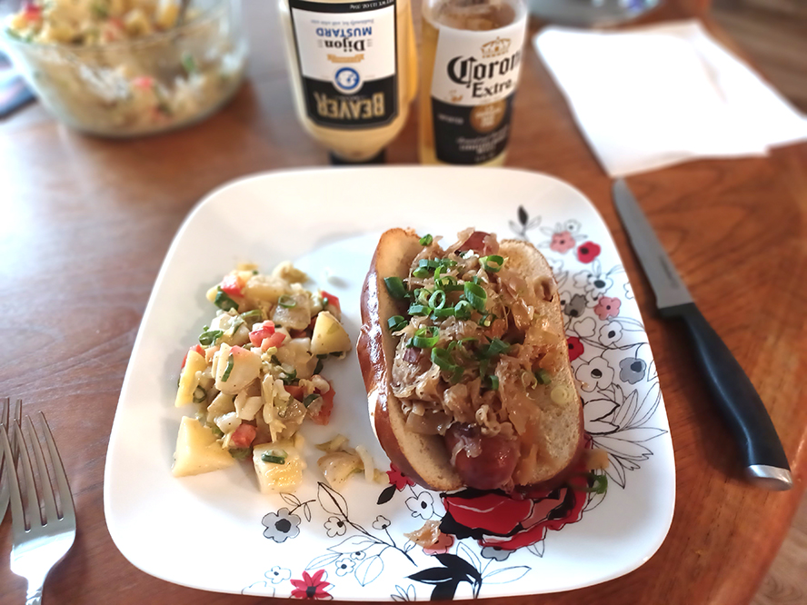 Warm or grill the pretzel bun, add the brat and the kraut mix, and potato salad. 